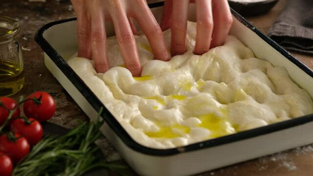 Female hands lay the dough in a baking tray, prepare Italian bread - focaccia with olive oil, tomatoes, seasonings, rosemary and sea salt. Dough for bread. Preparing focaccia - Pizza focaccia.