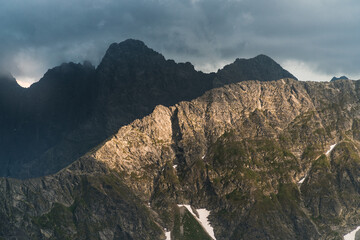 Fototapeta premium Dark cloudy sunset with light catching a little piece of rock. Dangerous conditions in Tatra Mountains with huge part covered with black shadow before heavy storm.