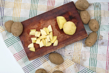 Pile of potato slice and unpeeled above wood cutting board