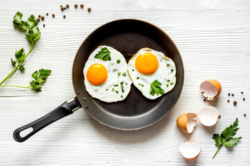Fried eggs on frying pan on white table top-down