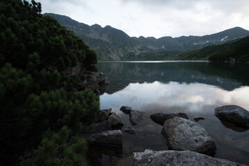 Hidden lake with reflection of mountains in it. Low clouds hanging above peaks.