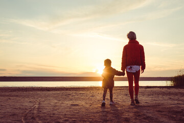 Silhouette of happy mother and little daughter at sunset. Back view of mother and young daughter standing and enjoying sunset  view