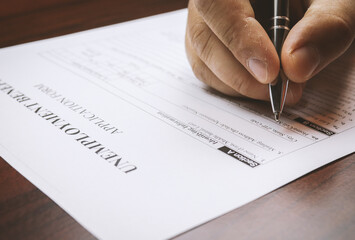 Close-up of a person's hand filing social security benefits application form.  Concept of coronavirus and stay at home order impact on economy. Selective focus, extremely shallow DOF.