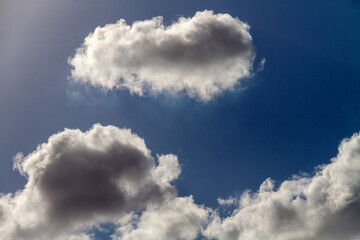 Naklejka na ściany i meble Beautiful puffy clouds in the rays of the sun on a blue sky.