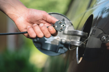Electric car concept. Electrical plug in driver hand on car background.