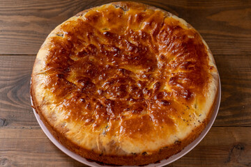 Freshly baked golden crust pie on a pink plate on a brown wooden table. Top-side view