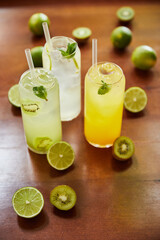 lemonade cocktails in glasses with straws and limes on wooden table, close view