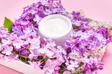 Jar of natural face cream with lilac flowers on pink background