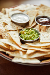  triangle-shaped corn chips with sauces, close view nachos and guacamole on plate