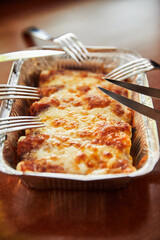 baked cheese dish in disposable rectangular tin paper aluminum foil bowl with forks and knives, close view