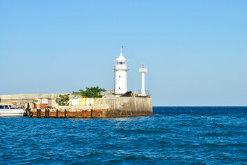 Fototapeta na wymiar White old lighthouse on pier near blue sea