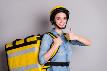 Stay home we take care tasty meal. Positive girl courier hold thermo container sushi recommend delivery service show thumb up sign wear helmet jeans shirt isolated gray color background