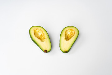 Two halves of fresh green pitted avocado cut on a white table
