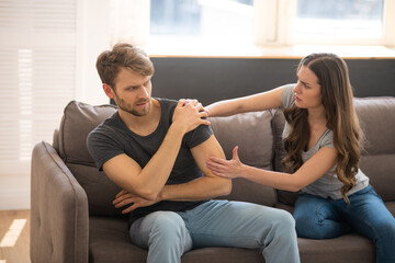 Obraz premium Long-haired young woman blaming her husband while he sitting with upset look