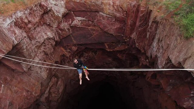 Scary pit under a man who is sitting on a slackline, massive pit, 4k