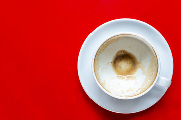 The top view of the empty coffee in a white cup with milk froth on a red table