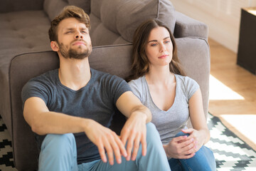 Young pretty woman and her husband sitting on the floor and looking frustrated