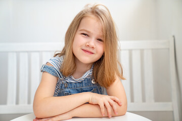 Naklejka premium Little girl in denim sits on white bench at table. bright workplace for child