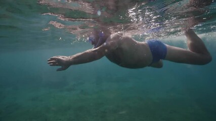 Underwater view of retired old man swimming in the clear ocean on sunny day.