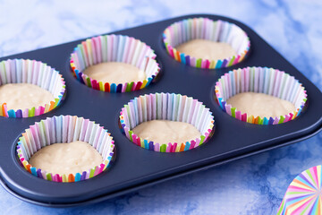 Metal cupcake baking dish with dough and paper cupcake molds.