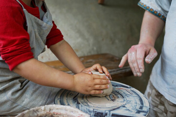 
little student makes a ceramic cup on a potter's wheel in a master class