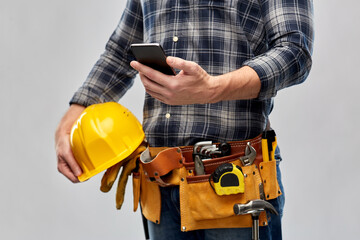 repair, construction and building - male worker or builder with smartphone and working tools on belt over grey background