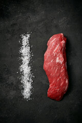 Raw beef tenderloin or bavet steak with salt on a dark stone background