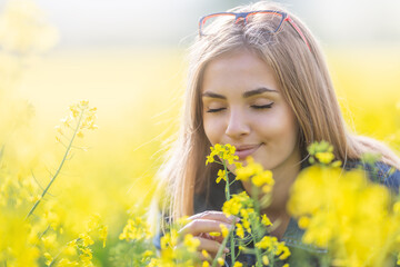 Beautiful young girl smells yellow flowers on a meadow with her eyes closed, smiling
