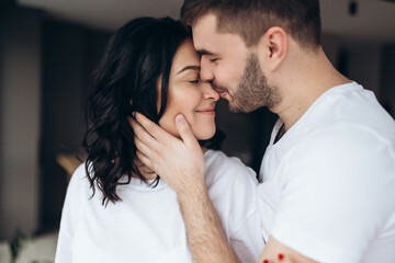 Stunning sensual intdoor portrait of young stylish fashion couple in love. Woman and man embrace and want to kiss each other. They are smiling and looking to each other