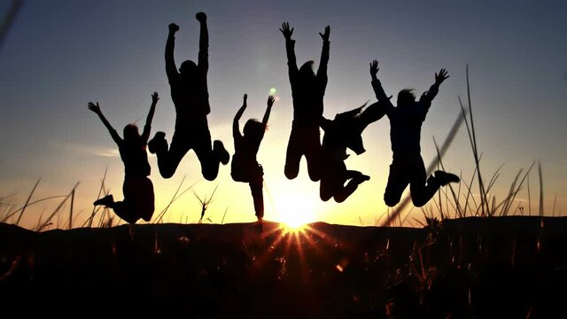 Silhouette of group friends that jumping together on the hilltop and raising hands to the sky