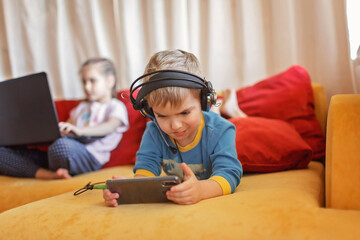 Gadget dependence, digital native generation alpha, kid lying on sofa and using gadgets at home