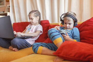 Gadget dependence, digital native generation alpha, kid lying on sofa and using gadgets at home
