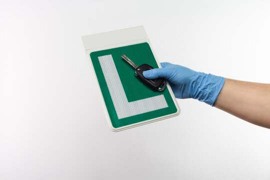 Person with protective gloves holding sign of Spanish driving school with car keys, covid-19 pandemic prevention 
 - Powered by Adobe