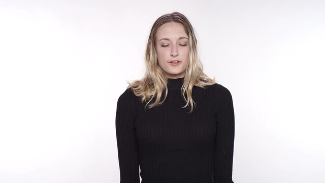 Young caucasian woman with blonde hair gives a namaste and breathes deeply on a white studio backdrop