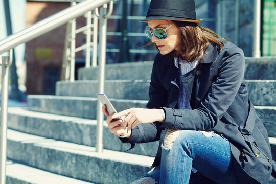 outdoor portrait of a stylish woman in hat and sunglasses with smartphone.