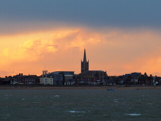 Orange sunset with clouds parting after a stormy day over St Nicholas Church on the seafront, Harwich, Suffolk, UK