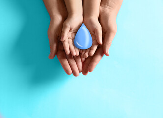Mother and her child holding water drop on light blue background, top view. Ecology protection