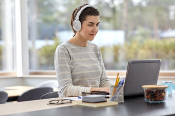 Obraz premium remote job, technology and people concept - happy smiling young woman in headphones with laptop computer working at home office
