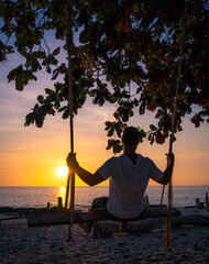 Man on a swing at sunset on the beach.
