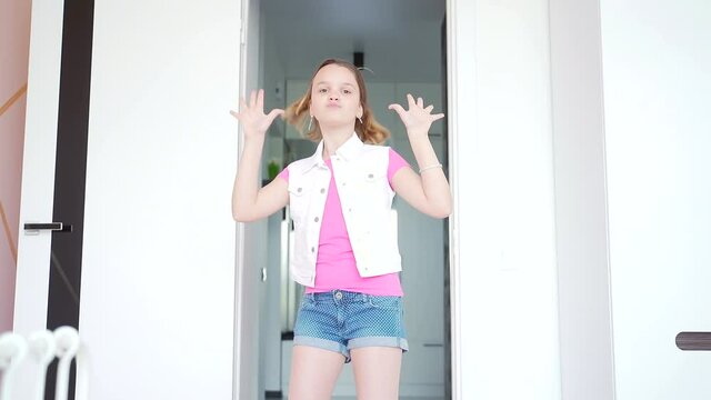
little teen girl dancing in front of the camera in the room, happy in denim shorts and stylish clothes. The child waves his arms happily jumps. slow motion