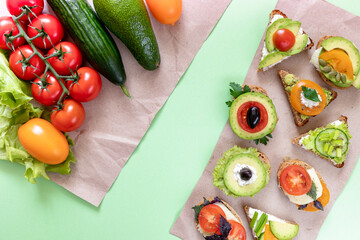 Vegetables and  sandwiches are lying on wrapping paper pieces on green background.