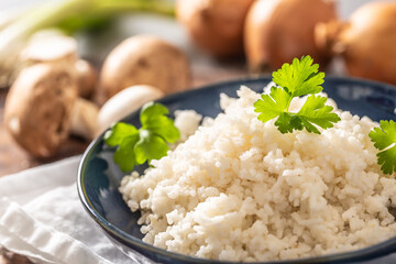 Bowl of steamed rice and parsley tops with mushrooms and leaks in the background