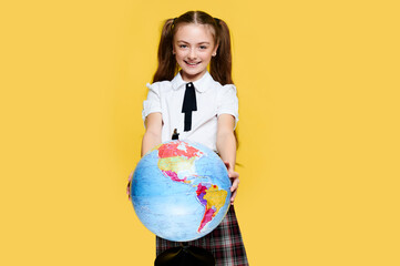 Elementary schoolgirl holding globe on yellow background, pupil with earth map