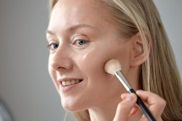 Blue-eyed blonde girl with a cosmetic brush. Close-up.