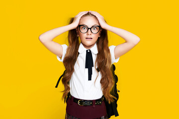 Surprised schoolgirl wearing uniform and glasses with backpack on vivid bright yellow background, caucasian elementary pupil, education school concept
