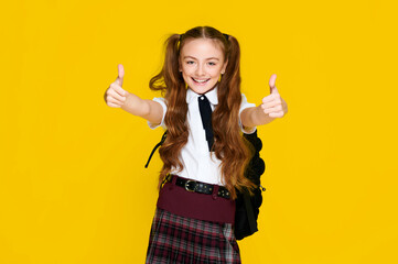 Elementary excited happy schoolgirl on vibrant yellow background showing thumb up on bright vibrant yellow background and smiling