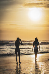 Fototapeta premium Two girls walking on the beach of Semyniak in Bali at sunset