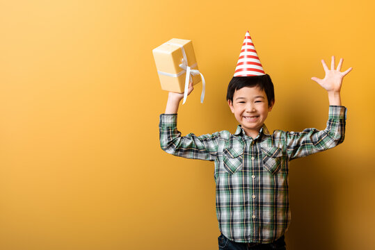 Happy Asian Boy In Birthday Party Cone Holding Present On Yellow