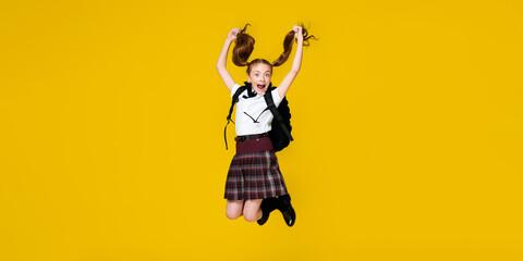 Fototapeta na wymiar Secondary school happy pupil jump in uniform with backpack on vibrant yellow background, back to school, learning education concept, banner format