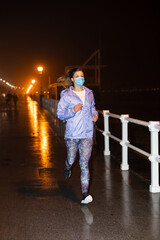 Sporty young woman runnning at night in the city wearing face mask against Covid-19. Gijon, Asturias, Spain.